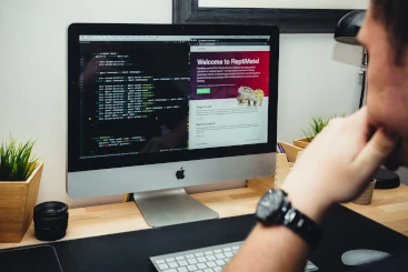 Image illustrant un individu en pleine réflexion devant un écran d'ordinateur. Sur celui-ci, on peut distinguer un code à gauche et une page web à droite. 